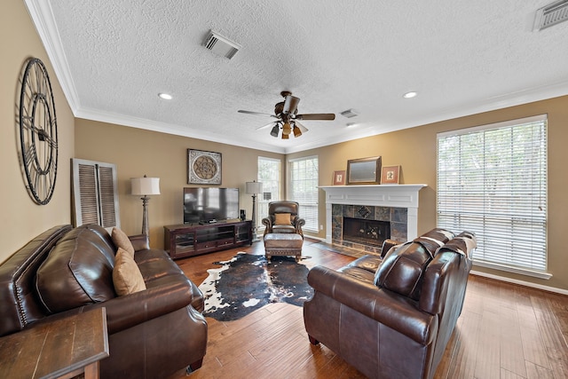 living room featuring wood-type flooring, a tiled fireplace, ornamental molding, and plenty of natural light