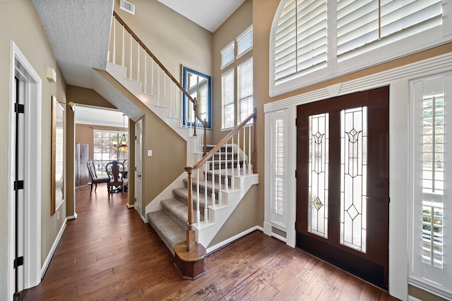 entrance foyer with a high ceiling, dark hardwood / wood-style flooring, a notable chandelier, and a wealth of natural light