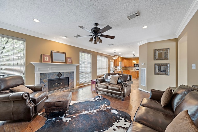 living room with a textured ceiling, a fireplace, ornamental molding, ceiling fan, and light hardwood / wood-style flooring