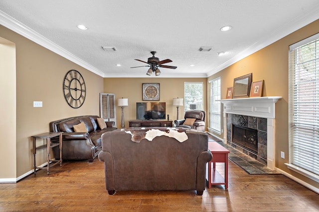 living room with hardwood / wood-style flooring, ceiling fan, ornamental molding, and a tile fireplace