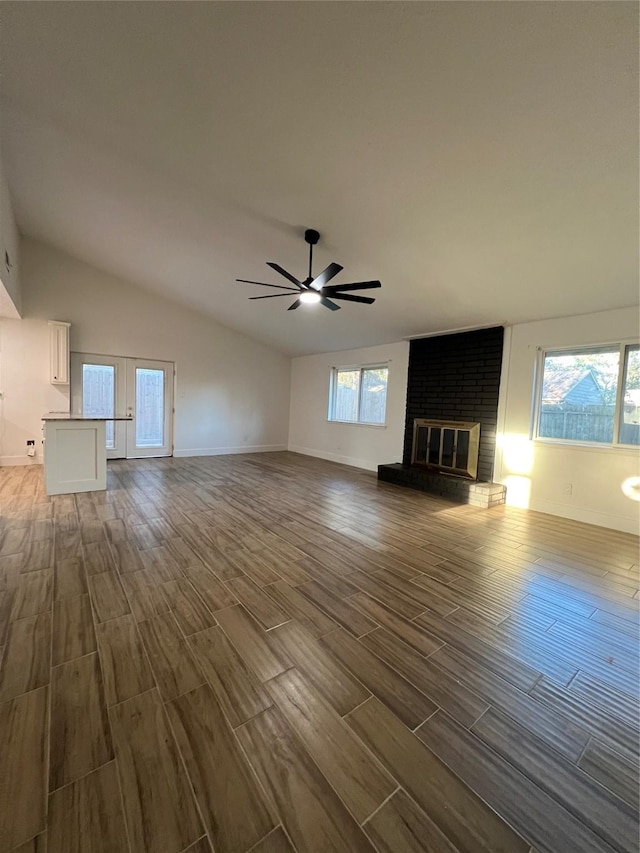 unfurnished living room with ceiling fan, french doors, a brick fireplace, and vaulted ceiling