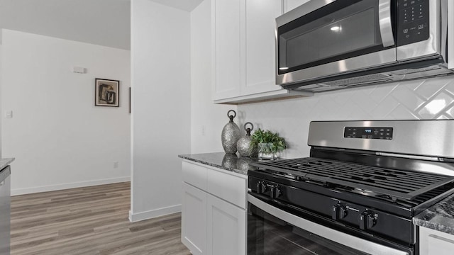 kitchen with white cabinets, stainless steel appliances, dark stone counters, and light hardwood / wood-style flooring