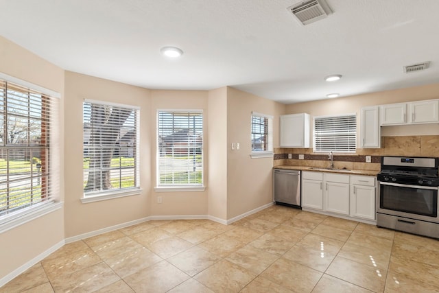 kitchen with appliances with stainless steel finishes, light tile patterned floors, sink, white cabinets, and tasteful backsplash