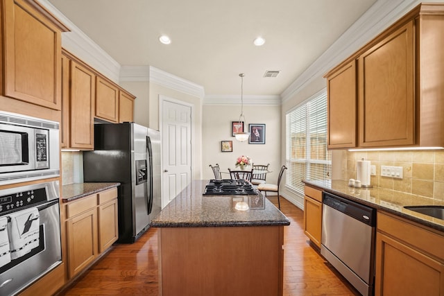 kitchen with hardwood / wood-style flooring, hanging light fixtures, a center island, dark stone counters, and appliances with stainless steel finishes