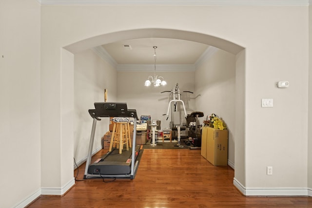 exercise room featuring wood-type flooring, an inviting chandelier, and ornamental molding