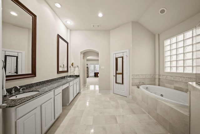 bathroom with tile patterned flooring, tiled bath, lofted ceiling, and vanity