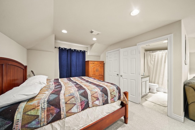 bedroom featuring lofted ceiling, ensuite bathroom, light colored carpet, and a closet