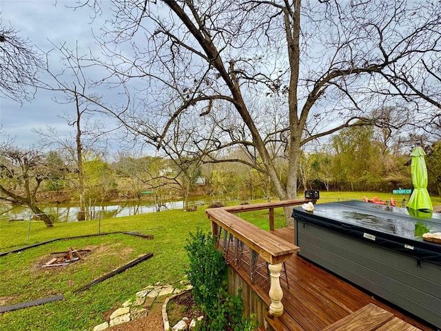 wooden terrace with a hot tub, fence, a water view, an outdoor fire pit, and a lawn