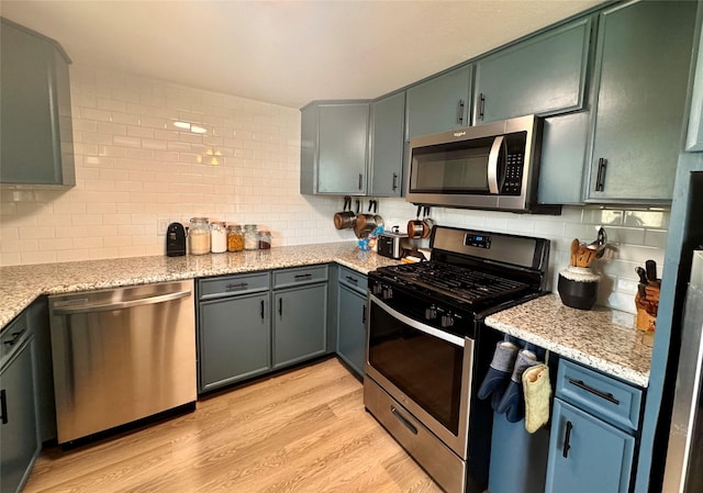 kitchen with tasteful backsplash, light wood-style flooring, appliances with stainless steel finishes, and light stone countertops