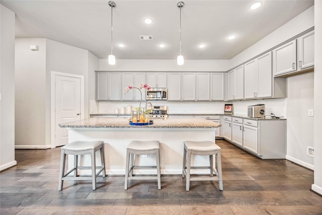 kitchen with light stone countertops, hanging light fixtures, a center island with sink, a kitchen bar, and appliances with stainless steel finishes