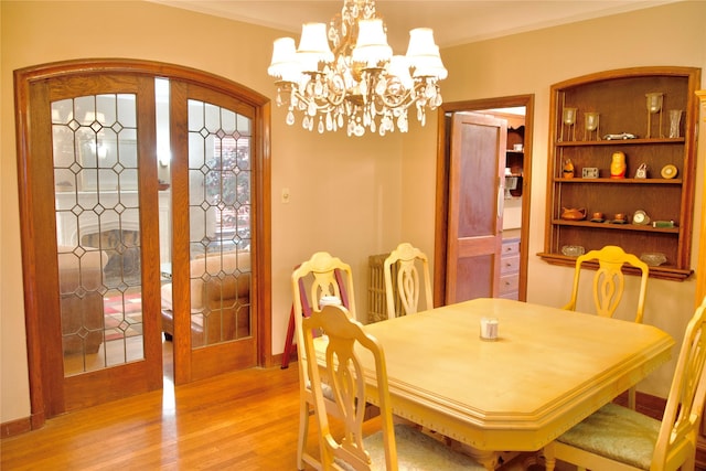 dining space featuring french doors, light hardwood / wood-style floors, crown molding, and a chandelier