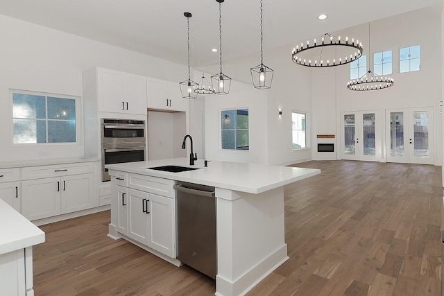 kitchen featuring a kitchen island with sink, appliances with stainless steel finishes, hanging light fixtures, sink, and white cabinetry