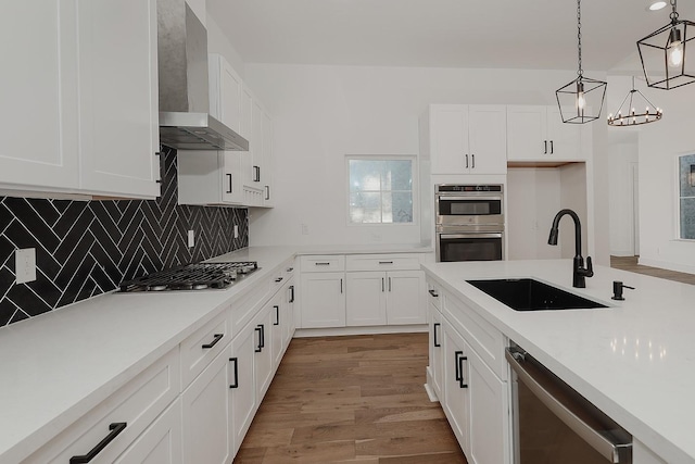 kitchen featuring wall chimney exhaust hood, hanging light fixtures, white cabinets, appliances with stainless steel finishes, and sink