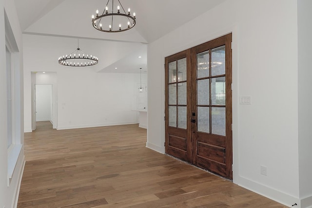 foyer entrance with french doors, wood-type flooring, vaulted ceiling, and a notable chandelier