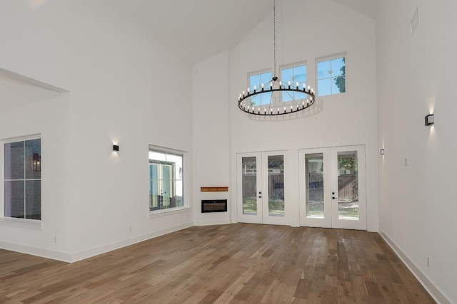 unfurnished living room with a high ceiling, french doors, hardwood / wood-style floors, and a notable chandelier