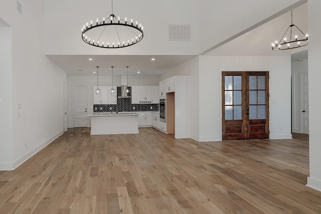 unfurnished living room featuring a high ceiling, light wood-type flooring, and french doors