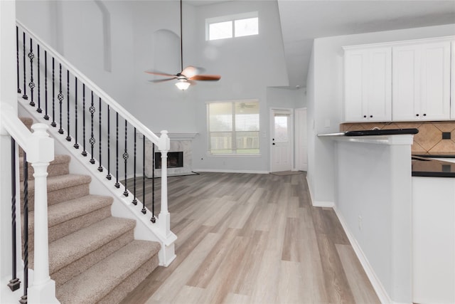 entryway with a towering ceiling, a high end fireplace, light wood-type flooring, and ceiling fan