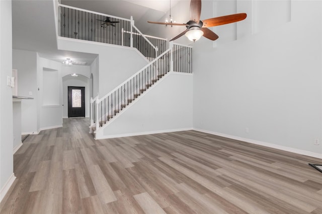 unfurnished living room with a high ceiling, ceiling fan, and light hardwood / wood-style floors