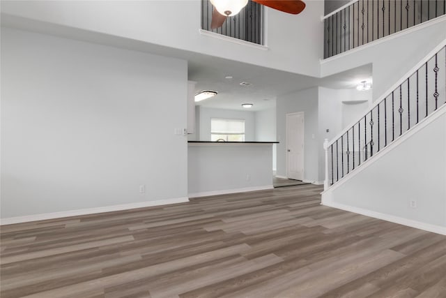 unfurnished living room with ceiling fan, hardwood / wood-style floors, and a towering ceiling