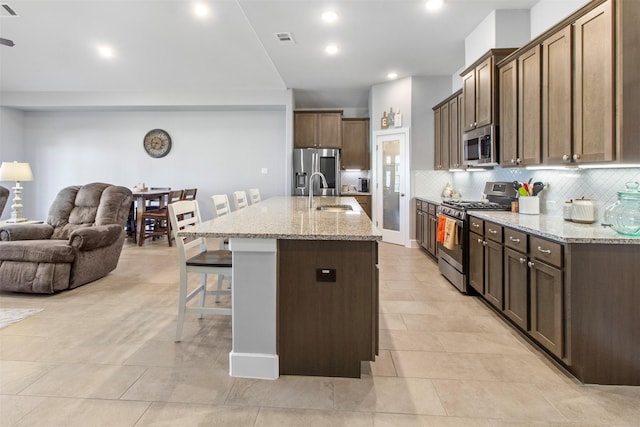 kitchen featuring sink, a kitchen breakfast bar, light stone countertops, a center island with sink, and appliances with stainless steel finishes