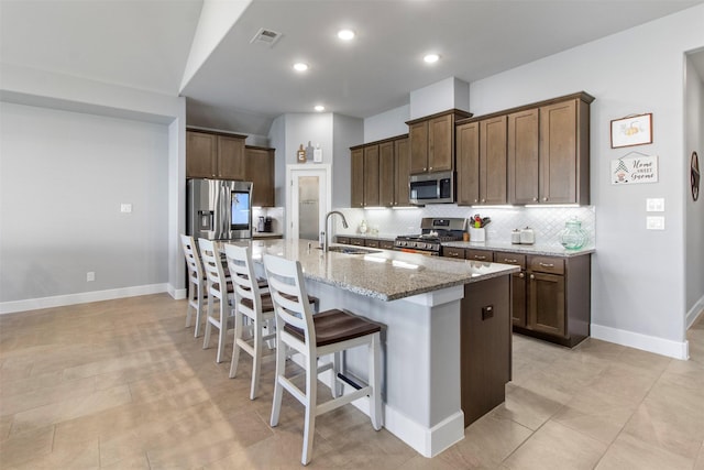 kitchen featuring light stone countertops, stainless steel appliances, a center island with sink, a kitchen breakfast bar, and sink