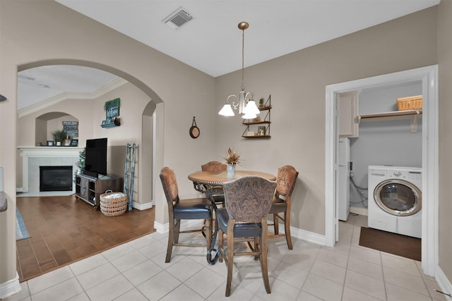 tiled dining space with washer / clothes dryer, a tiled fireplace, ornamental molding, and an inviting chandelier