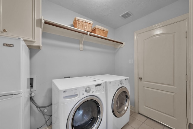 clothes washing area featuring a textured ceiling, cabinets, washer and clothes dryer, and light tile patterned floors