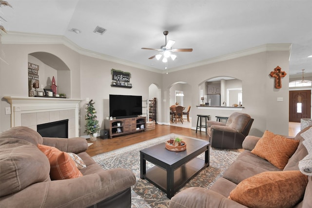 living room featuring ornamental molding, ceiling fan, a tile fireplace, and wood-type flooring