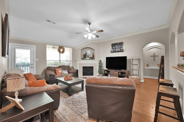 living room featuring ceiling fan, a tiled fireplace, light hardwood / wood-style flooring, and crown molding