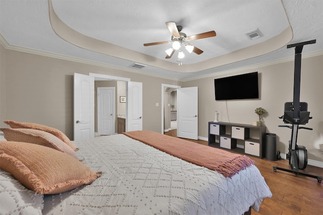 bedroom featuring ensuite bathroom, a raised ceiling, ceiling fan, wood-type flooring, and crown molding