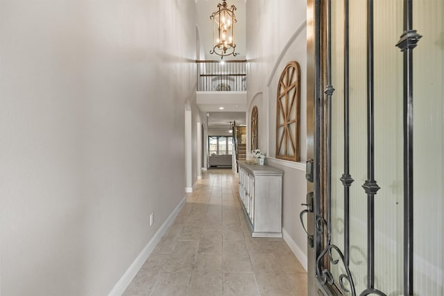 hallway featuring a high ceiling, an inviting chandelier, and light tile patterned floors