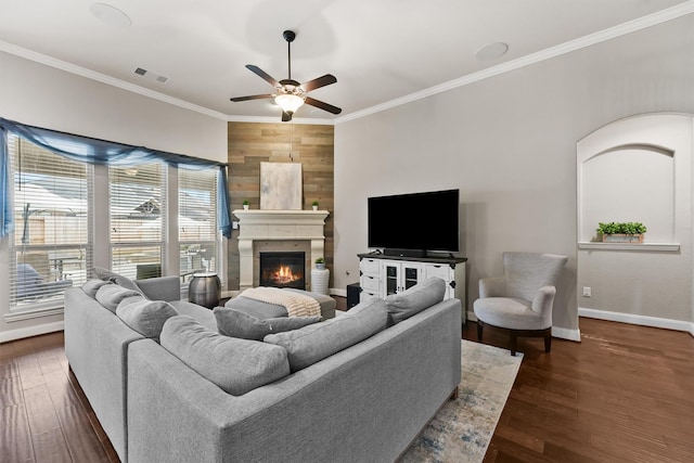 living room with a large fireplace, wood walls, crown molding, ceiling fan, and dark wood-type flooring