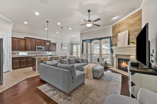 living room featuring a fireplace, ceiling fan, crown molding, and sink