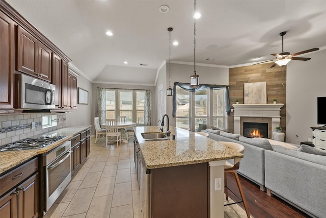 kitchen with sink, stainless steel appliances, wood walls, a center island with sink, and pendant lighting