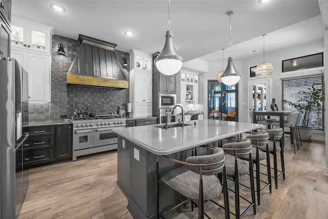 kitchen with stainless steel appliances, custom range hood, pendant lighting, decorative backsplash, and white cabinetry