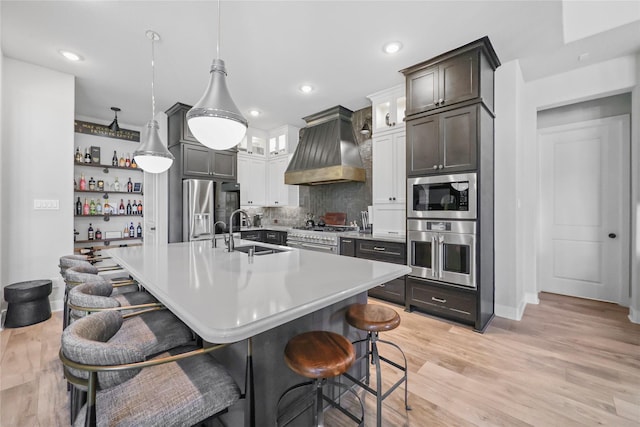 kitchen with sink, decorative light fixtures, wall chimney exhaust hood, a breakfast bar, and appliances with stainless steel finishes