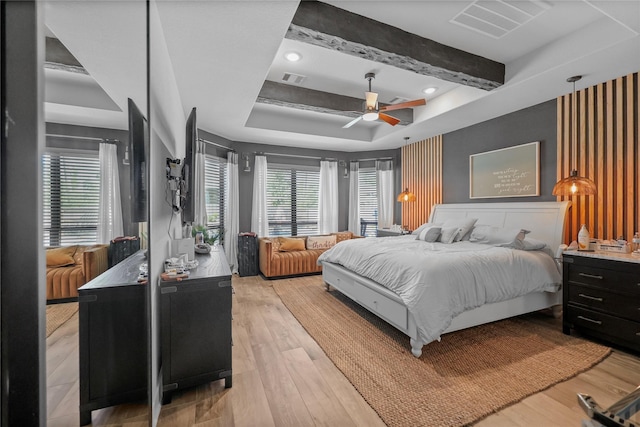 bedroom with multiple windows, ceiling fan, a tray ceiling, and light hardwood / wood-style flooring