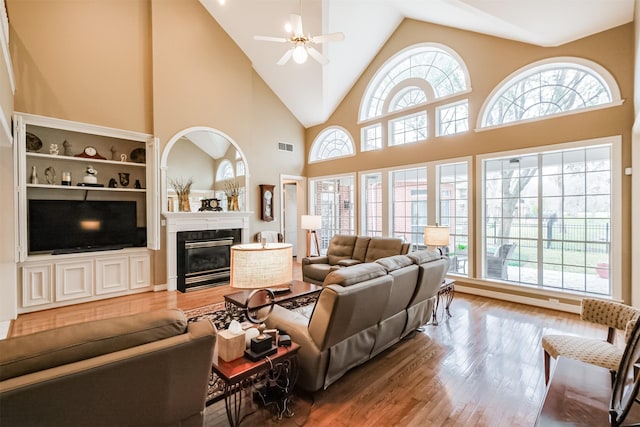 living room featuring ceiling fan, high vaulted ceiling, wood finished floors, visible vents, and a glass covered fireplace