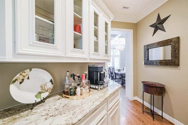 bar with white cabinetry, light stone countertops, light hardwood / wood-style flooring, and ornamental molding