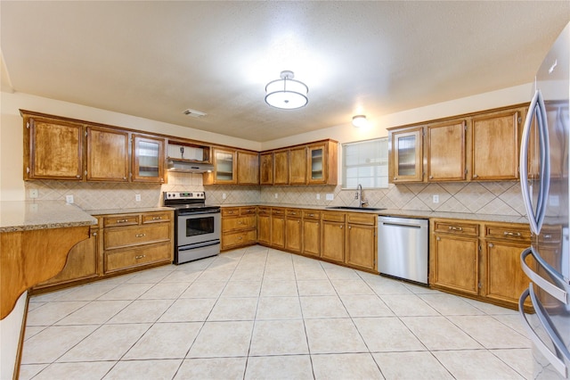 kitchen with appliances with stainless steel finishes, light stone countertops, sink, and light tile patterned floors