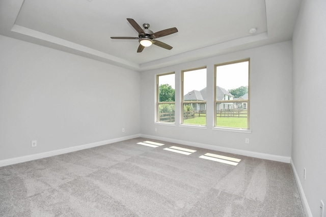 carpeted empty room with a raised ceiling and ceiling fan