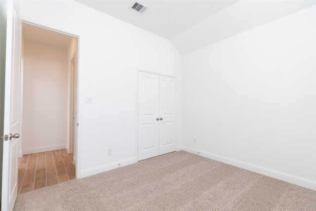 unfurnished bedroom with baseboards, visible vents, light colored carpet, vaulted ceiling, and a closet