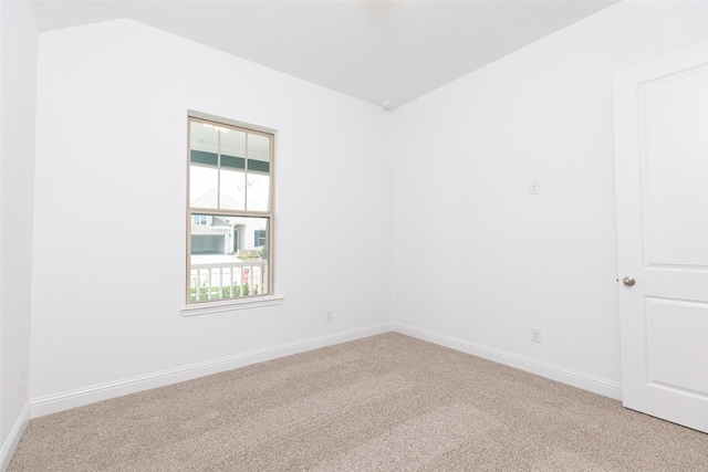 empty room with lofted ceiling, light colored carpet, and baseboards