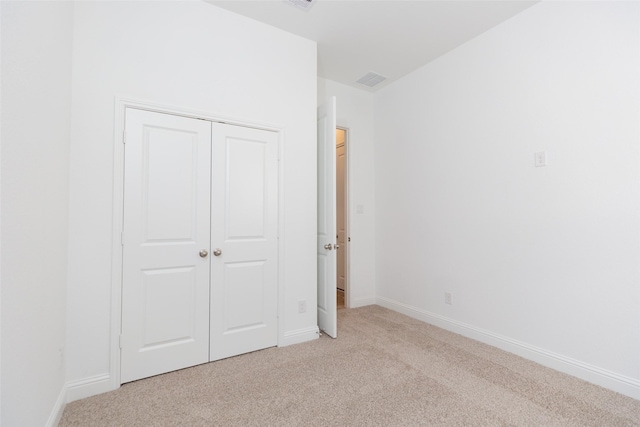 unfurnished bedroom with a closet, light carpet, and baseboards