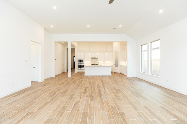 unfurnished living room featuring light wood finished floors, baseboards, vaulted ceiling, and recessed lighting