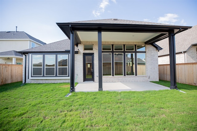 rear view of property featuring a patio, a fenced backyard, brick siding, a shingled roof, and a lawn