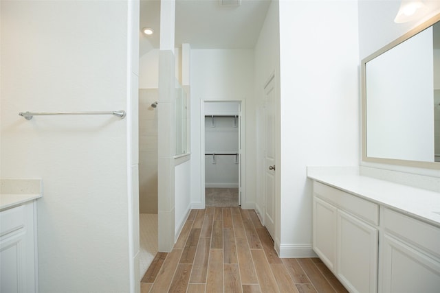 bathroom with a spacious closet, walk in shower, wood finished floors, and vanity