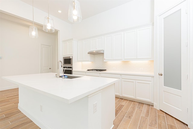 kitchen with appliances with stainless steel finishes, wood finish floors, under cabinet range hood, and tasteful backsplash