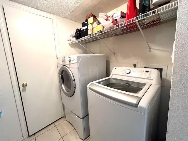 clothes washing area with a textured ceiling, washing machine and dryer, and light tile patterned floors