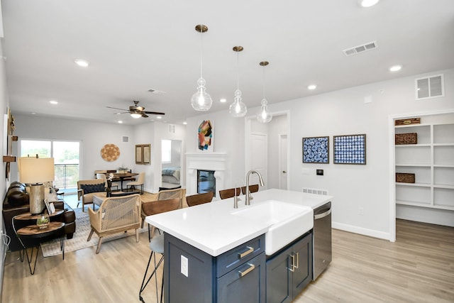 kitchen featuring sink, a kitchen bar, ceiling fan, an island with sink, and hanging light fixtures